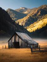 Rustic Wooden Barn in a Mountain Valley at Sunrise. A solitary barn stands in a field of tall grass, with majestic mountains and a forest in the background. photo