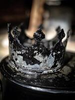 Close Up of a Weathered Black Crown on a Dark Surface. photo