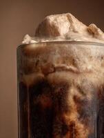 Close Up of a Frothy Brown Soda Drink in a Glass. A Detailed Image Showing the Texture and Bubbles. photo