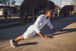 Muscular man trains outdoors in warm weather, working on his upper body strength through push ups in a sunny urban setting. photo