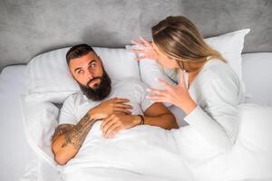 A young married couple yelling and frustrated during an intense argument while lying on their bed in a home setting. photo