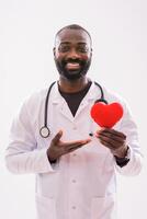 Smiling black male doctor in uniform with a stethoscope, showing a red heart shape as a sign of successful treatment and healing. photo