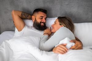 Couple lying close, exchanging smiles and enjoying a relaxed, carefree moment in their intimate space. photo