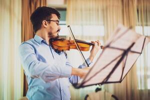 Portrait of a Caucasian man playing a violin in a cozy room, fully immersed in his music, wearing eyeglasses and expressing emotion. photo
