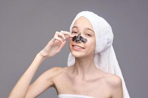 Young caucasian female applying blackhead mask with towel on head smiling skincare routine. photo