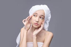 Young asian female applying under eye patches for skincare routine with towel wrapped around head. photo
