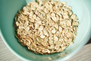 Close-up of raw oatmeal in a light blue bowl on wooden surface in sunlight. photo