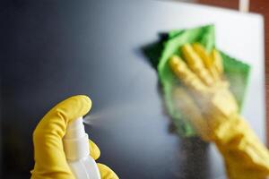 Close up of gloved hands cleaning screen with spray bottle and cloth for a streak free surface. photo