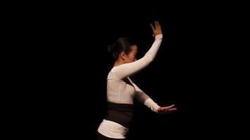 A dancer in a white outfit performs gracefully against a black background, showcasing expressive hand movements and body language. video
