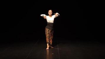 A dancer performing on stage, showcasing traditional attire with intricate patterns. The background is dark, highlighting the dancer's movements and elegance. video