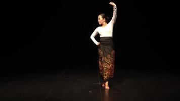 A dancer performing on stage in a dramatic pose, wearing a traditional outfit with intricate patterns. The background is dark, highlighting the dancer's movements and expression. video