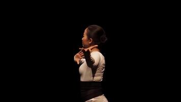 A dancer performing gracefully against a dark background, showcasing fluid movements and expressive body language. The focus is on the dancer's form and elegance. video