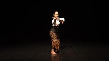 A dancer performing on stage, dressed in traditional attire with intricate patterns. The background is dark, highlighting the dancer's movements and grace. video