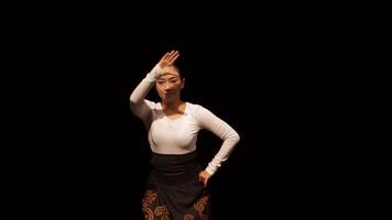 A dancer performing on stage, showcasing traditional attire and graceful movements. The background is dark, emphasizing the dancer's elegant pose and expression. video