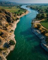 River flowing through rocky terrain and green fields under clear sky with distant mountains photo
