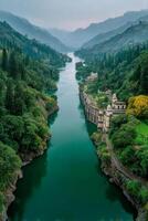 River flowing through lush green forest valley with dam and buildings surrounded by misty mountains in peaceful nature photo