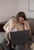 A mother skillfully multitasks at home with her baby nearby while using her laptop for work photo