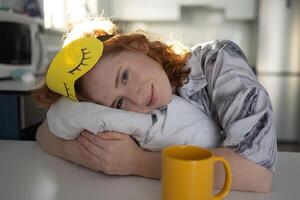 A woman with a sleep mask sits at a table with coffee photo