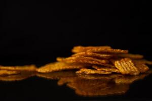 Golden ridged potato chips piled on a dark reflective surface, emphasizing their crispy texture and delicious snack appeal for a quick bite photo