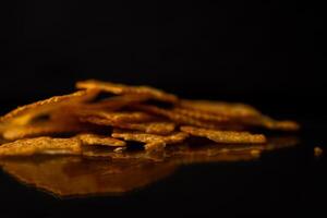A close-up of delicious golden crackers stacked with a crisp texture, casting a reflection on a sleek dark surface, highlighting savory snack food photo