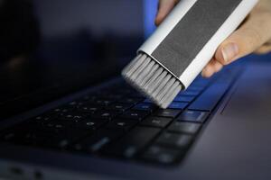 Person's hand cleaning a laptop keyboard with a specialized brush, ensuring thorough device maintenance and promoting a hygienic digital workspace photo