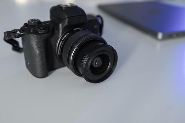 Professional black mirrorless camera with a lens resting on a clean white desk, symbolizing modern digital photography and videography for content creation