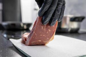 A person in a black glove carefully places a fresh raw beef steak onto a white paper towel, emphasizing hygiene and quality in kitchen food preparation photo