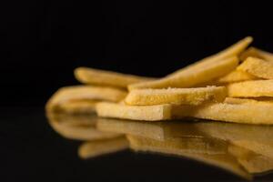 Uncooked golden frozen french fries with visible frost crystals, neatly stacked on a sleek dark reflective surface, highlighting fast food photo