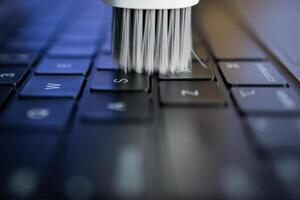 White cleaning brush sweeping across a laptop keyboard, symbolizing essential electronic device maintenance, ensuring longevity and efficient digital workflow for users photo