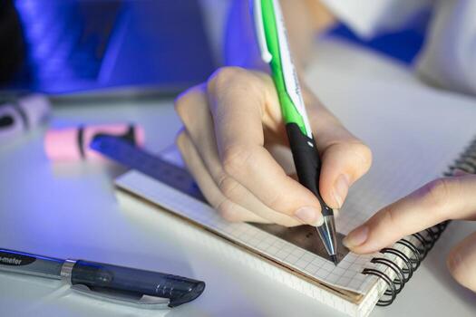 Student's hand diligently using a green pen and ruler on a grid notebook, illustrating academic precision, focused learning, and effective study methods photo