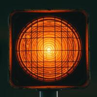 Close up of a bright orange traffic signal light with a protective grid against a dark background photo
