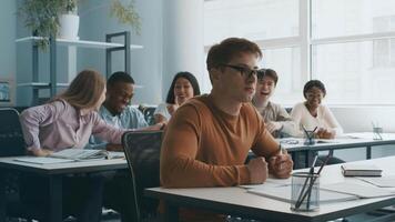 In a modern classroom, diverse college students collaborate while studying. Some share laughs, while others focus on their tasks, creating an engaging educational environment. video