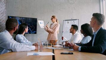 A group of professionals discusses business strategies in a modern office. A leader presents reports on growth, with team members engaged and taking notes while reviewing performance charts. video