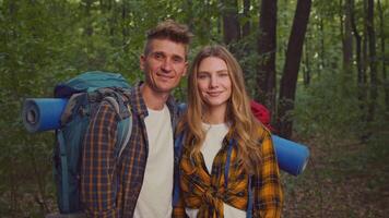 A couple stands together in a serene forest, ready to start their camping trip. Their backpacks are loaded with essentials as they embrace an active lifestyle amidst nature's beauty. video