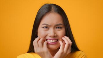 A young Asian woman with long hair displays a frustrated expression, clutching her face with her hands. The bright yellow backdrop emphasizes her emotion, capturing a relatable moment in lifestyle. video