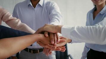 In a bright office environment, several professionals join hands in a gesture of teamwork and collaboration. video