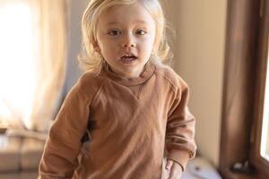 A three-year-old boy with blond curly hair is jumping on the couch at home photo