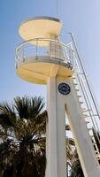 White lifeguard tower stands near palm trees in Alicante, Spain. Image suitable for beach safety, tourism, or coastal architecture context photo
