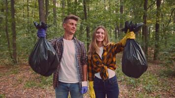 A couple stands together in a lush forest, both wearing gloves and holding bags for collecting trash. They promote an active lifestyle by participating in a community cleanup effort. video