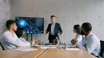 A group of professionals is engaged in a business meeting. The leader presents data on a screen while the team attentively listens. They are in a modern office setting. video