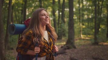 A young woman enjoys the beauty of the forest while hiking through the trees. She carries a backpack and smiles, embracing her active lifestyle surrounded by nature's greenery. video
