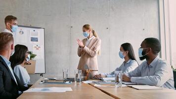 A business meeting takes place in a contemporary office, with a leader presenting ideas to her team. Everyone is engaged, wearing masks, and collaborating on a project, showcasing teamwork. video
