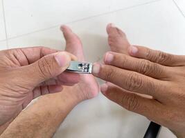 Cutting fingernails with clippers shows personal grooming and self-care at home on white tile. photo