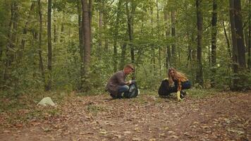 Two individuals participate in a forest clean-up, collecting litter to promote environmental health. They are dressed for outdoor work, surrounded by lush greenery in a serene forest setting. video