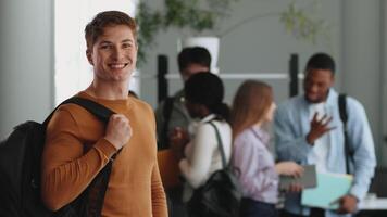 A smiling guy posing next to group of college students of various engage in a collaborative study session in a modern university setting. video