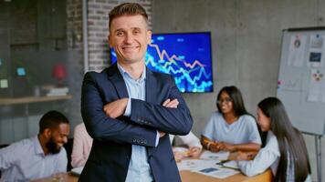 A confident professional stands in front of team members engage in discussion and planning at a meeting table nearby. video
