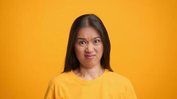 A millennial Asian woman makes a humorous face, conveying surprise or disgust, in a vibrant yellow setting. Her expression adds a playful touch to the overall visual impact. video