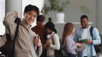 Students from various backgrounds collaborate and study in a lively university setting. One student Asian guy smiles while holding books, creating an inviting atmosphere of learning and friendship. video