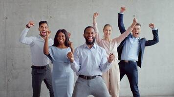A group of five multiethnic professionals poses together in a sleek office space with a concrete wall. They display confidence and unity, representing diversity in business success and collaboration. video