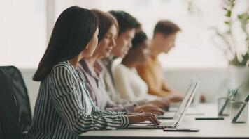A diverse group of students is focused on their laptops while studying together in a bright, modern university setting. They are collaborating and sharing ideas for their coursework. video